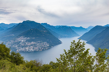 Aerial panorama view of Lugano Lake, cityscape of Lugano, mountain Monte Bre and Swiss Alps mountain range on a cloudy summer day from top of Monte San Salvatore, Canton of Ticino, Switzerland