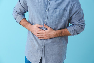 Young man suffering from abdominal pain on color background