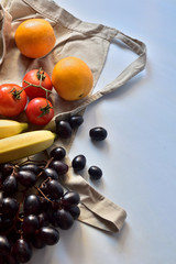 Fresh natural fruits, on an apron, light blue background. Oranges, tomatoes, bananas and black grapes. Natural lighting, space to write.