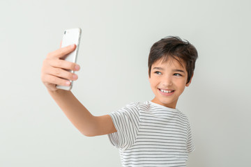 Cute little boy taking selfie on light background