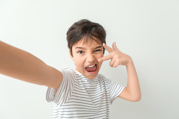 Cute little boy taking selfie on light background