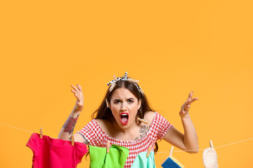 Angry housewife with laundry on color background