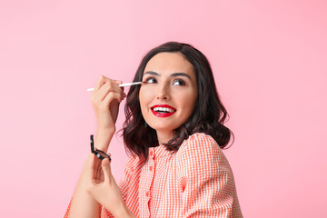 Obraz premium Beautiful young woman applying makeup on color background