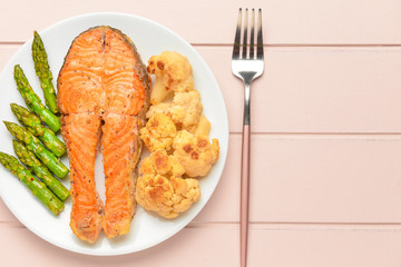 Plate with fried salmon and vegetables on table