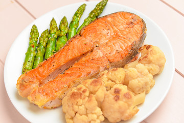 Plate with fried salmon and vegetables on table, closeup