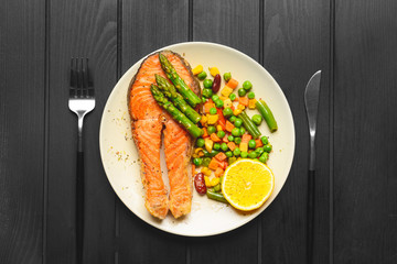Plate with fried salmon and vegetables on table