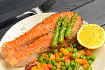 Plate with fried salmon and vegetables on table, closeup