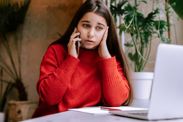 upset woman talking on phone and holding head. Young businesswoman sitting in office, working on computer. Online marketing, business education for adult, teleworking