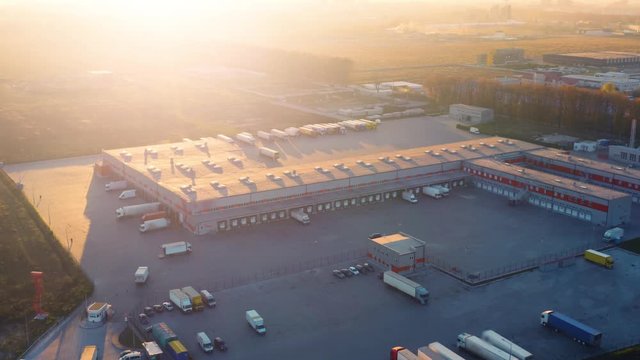 Aerial view of the logistics park with warehouse, loading hub and semi trucks with cargo trailers standing at the ramps for load/unload goods at sunset