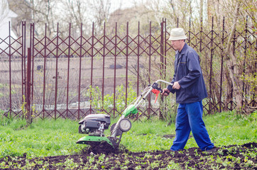 A man plows the land with a cultivator in a spring garden