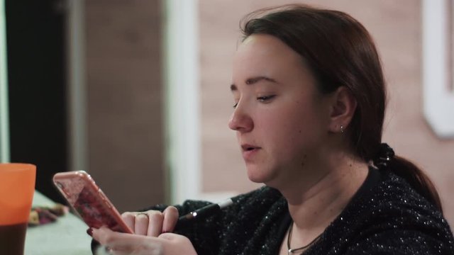 Close-up. Girl smokes iqos, electronic cigarette, using smartphone texting, messaging on social networks, enjoying mobile technology, standing bar house, private party, holiday. Evening, New Year
