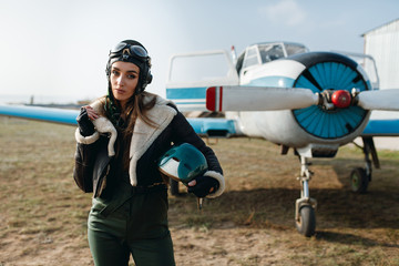 a girl in a headdress with glasses in a leather jacket with fur holds in his hand a pilot's helmet,...