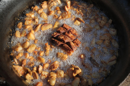 Pork greaves preparing in a big pot, tasty snacks in hot fat made from bacon