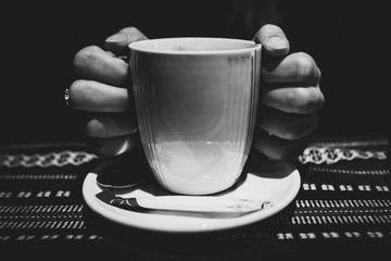 czarno białe zdjęcie kobiecych dłoni na kubku czarnej kawy