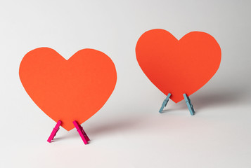 Two paper hearts stands on wooden clothespins on white background. Minimal love concept.