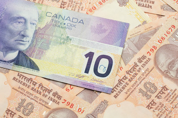 A macro image of a purple Canadian ten dollar bill on a background of Indian ten rupee bank notes close up
