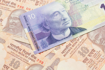 A macro image of a purple Canadian ten dollar bill on a background of Indian ten rupee bank notes close up