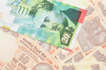 A close up image of a twenty shekel bank note from Israel on a background of Indian ten rupee bank notes in macro