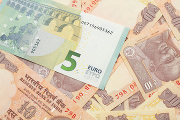 A close up image of a five Euro bank note from Europe in macro with a bed of Indian ten rupee bank notes