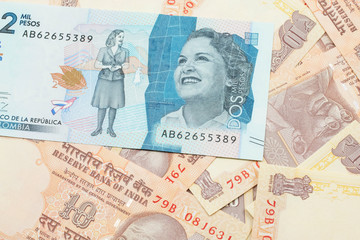 A close up image of a blue two thousand Colombian peso bank note on a background of Indian ten rupee bank notes in macro