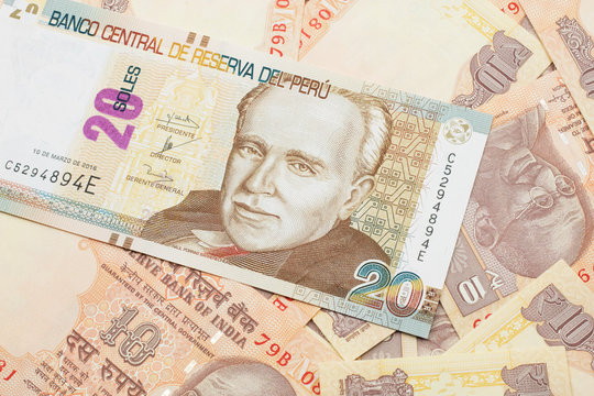 A close up image of a new, Peruvian twenty sol bank note close up on a bed of Indian ten rupee bank notes in macro