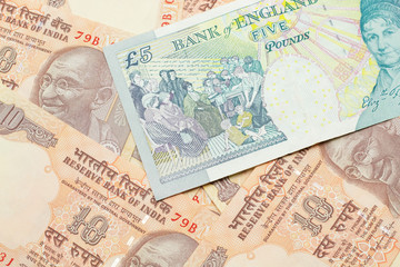 A close up image of a multicolored five pound note from the United Kingdom on a background of Indian ten rupee bank notes in macro