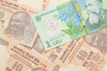 A close up image of a green Romanian one leu bank note on a background of Indian ten rupee bank notes