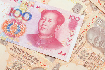 A close up image of a red, one hundred Chinese yuan bank note, close up on a background of orange Indian ten rupee bank notes.  Shot in macro