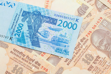 A close up image of a blue, two thousand, West African franc bank note in macro on a background of United States one dollar bills