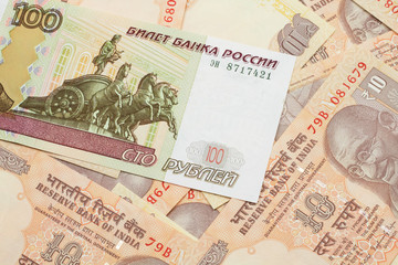 A close up image of a one hundred ruble bank note on a background of orange, ten Indian rupee notes from India.  Shot close up in macro