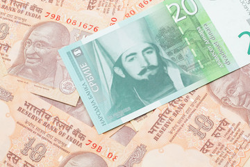 A close up of a green and white, twenty Serbian dinar bank note on a background of Indian ten rupee bank notes