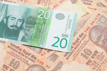 A close up of a green and white, twenty Serbian dinar bank note on a background of Indian ten rupee bank notes