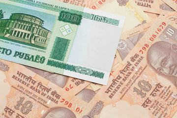A green hundred ruble bank note from Belarus on a bed of Indian ten rupee bank notes close up in macro