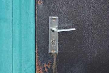 one gray metal doorknob on a brown iron dirty door and a green wall on the street