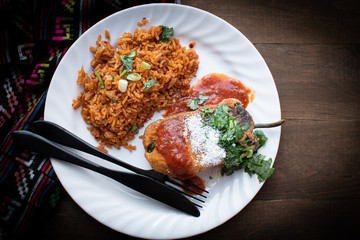 Chiles rellenos and Mexican rice in white dish on wooden table