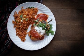 Chiles rellenos and Mexican rice in white dish on wooden table