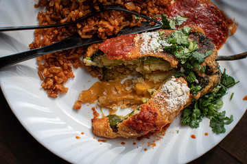 Chiles rellenos and Mexican rice in white dish on wooden table