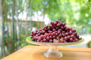 red grape on the step glass plate stand alone on the wood table in the outdoor garden field blur bokeh.