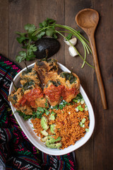 Chiles rellenos and Mexican rice in white dish on wooden table
