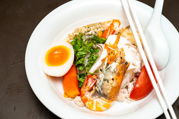 Seafood Thai noodle mixxed together between boiled shrimp, squid, pork, egg and colourful vegetable in white bowl.