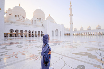 Traveling by Unated Arabic Emirates. Woman in traditional abaya standing in the Sheikh Zayed Grand Mosque, famous Abu Dhabi sightseeing. - obrazy, fototapety, plakaty