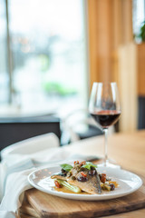 Grilled fish on white plate and wine glasses.