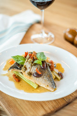 Grilled fish on white plate and wine glasses.