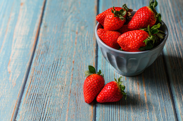 Blue beautiful organic strawberries in a blue bowl on a blue wooden background.