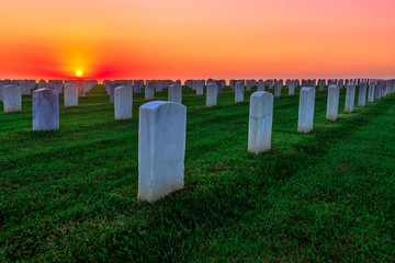 National cemetery with rows of white gravestones. The sunset sun above the ocean in San Diego Bay...