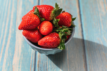 Blue beautiful organic strawberries in a blue bowl on a blue wooden background.