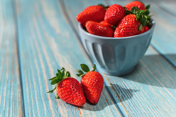 Blue beautiful organic strawberries in a blue bowl on a blue wooden background.