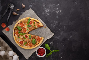 Pizza Margarita with cherry tomatoes, Basil leaves and mozzarella cheese on a dark concrete background. Without one slice of pizza