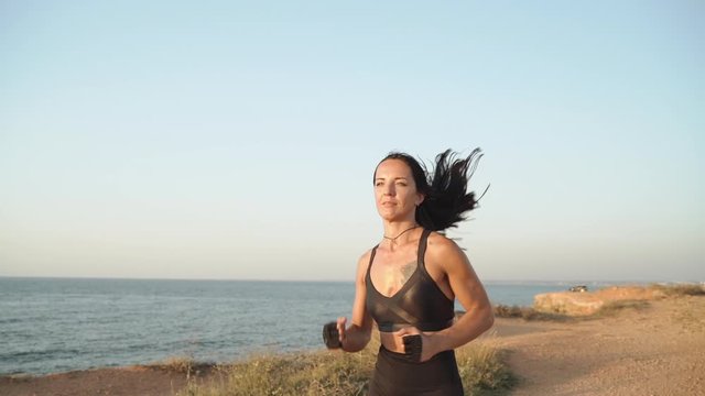 Young adult sportswoman training outdoors, running near sea