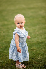 Adorable blue-eyed baby girl in a beautiful blue dress stands barefoot on the grass